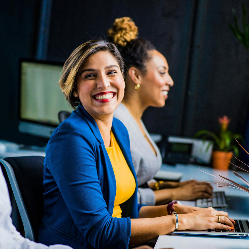 Women smiling and working on desktop computers