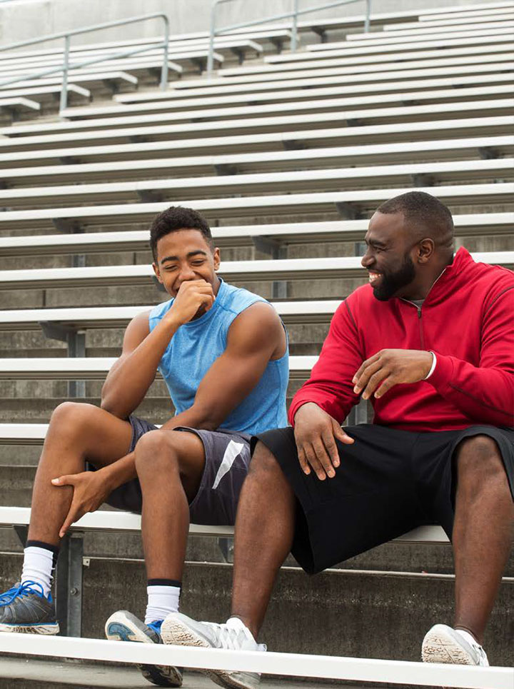 A man and a teen in joyful conversation on outdoor bleachers